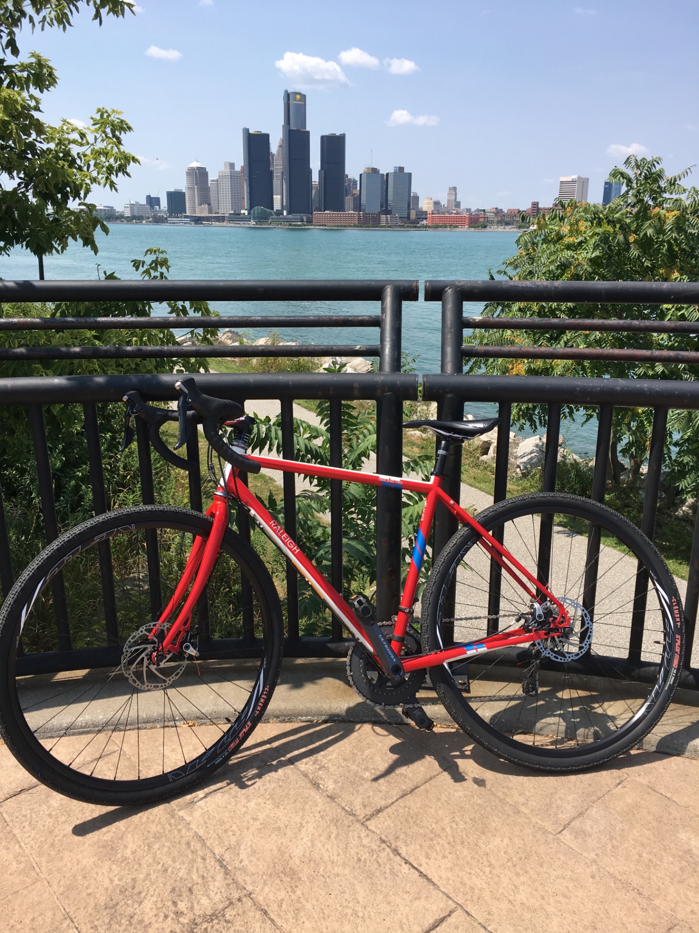 Eric's red Raleigh Tamland adventure bicycle leaning against a railing along the Detroit River in Windsor, Ontario, with the Detroit skyline across the water