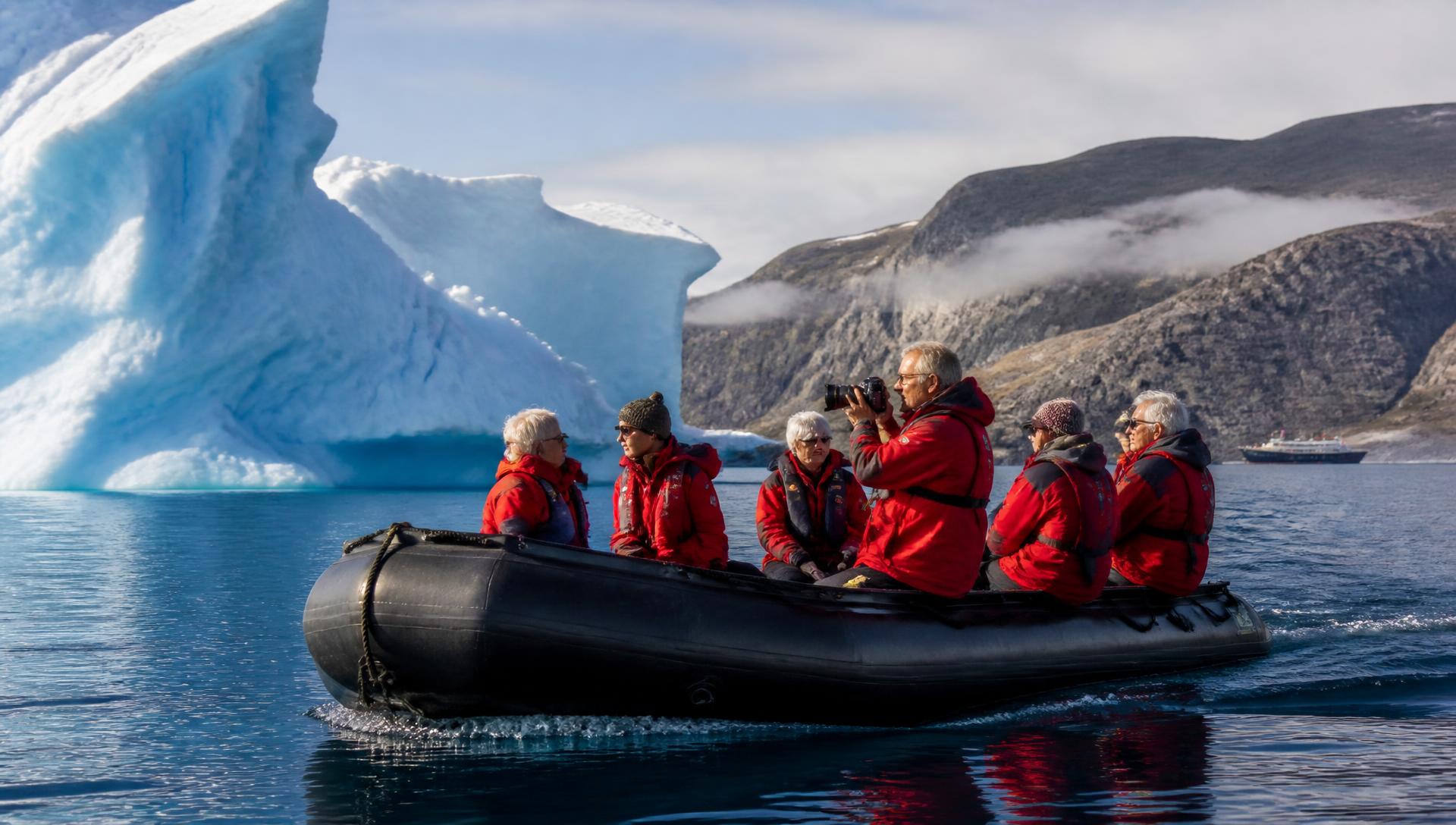 Active adults in expedition parkas exploring a remote polar coastline by Zodiac, a towering blue iceberg beside them.